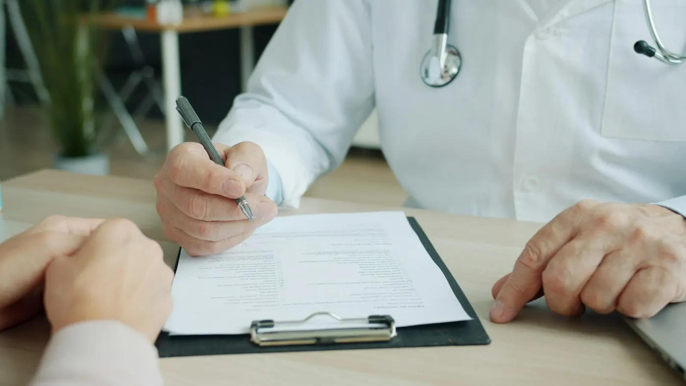 Médico do trabalho preenchendo e assinando o ASO em uma prancheta, diante do colaborador